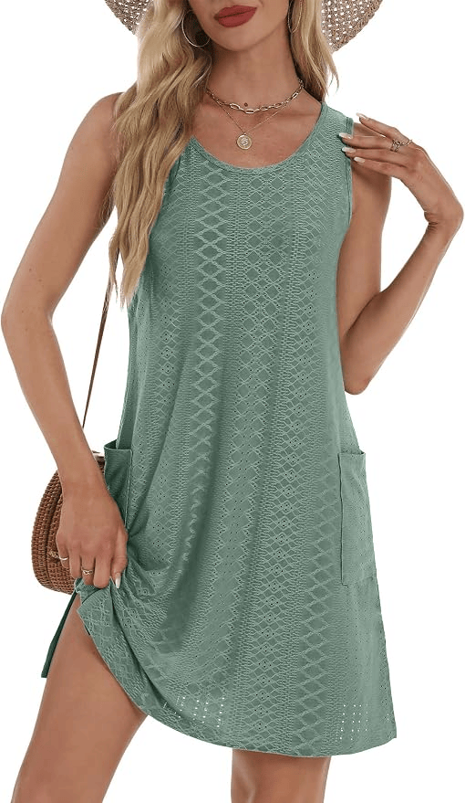 A woman wearing a sleeveless green dress with a textured pattern and pockets, styled with a wide-brimmed hat and a woven handbag.