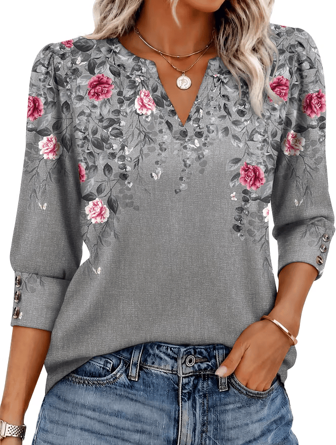A woman wearing a gray floral blouse with pink roses and green leaves, featuring a V-neck and three-quarter sleeves, paired with blue jeans.