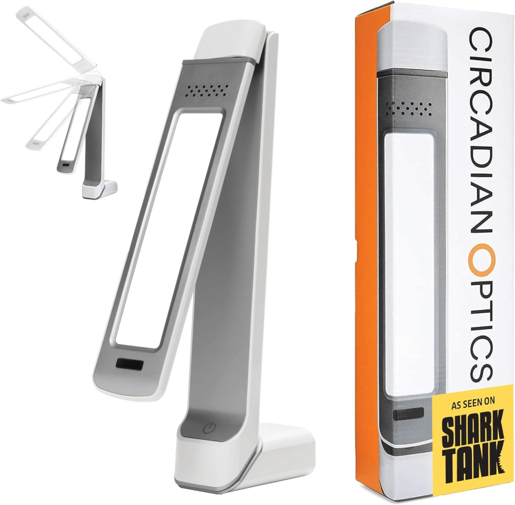 A modern adjustable desk lamp in gray and white, featuring a minimalist design with an on/off button at the base. The lamp is shown next to its packaging, which includes a logo stating 'As Seen on Shark Tank.'