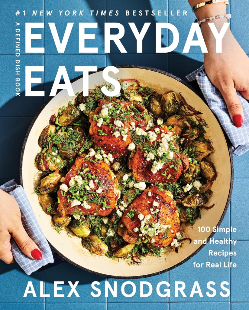 Cover of the cookbook 'Everyday Eats' by Alex Snodgrass, featuring a dish of chicken thighs and Brussels sprouts, garnished with herbs and cheese, on a blue background.